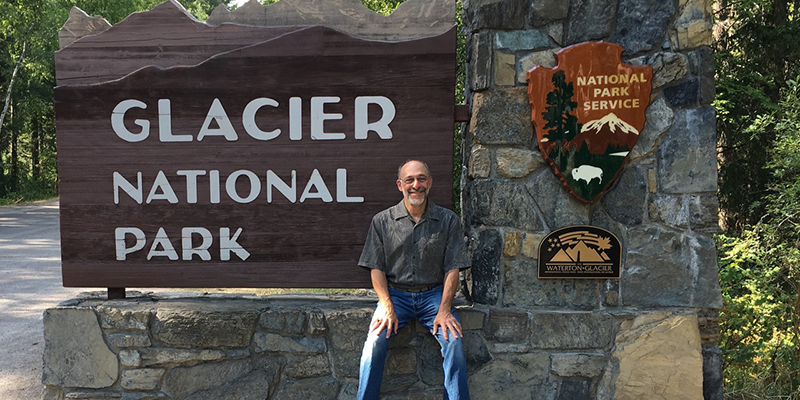 Howard Stolz sitting next to Glacier National Park sign
