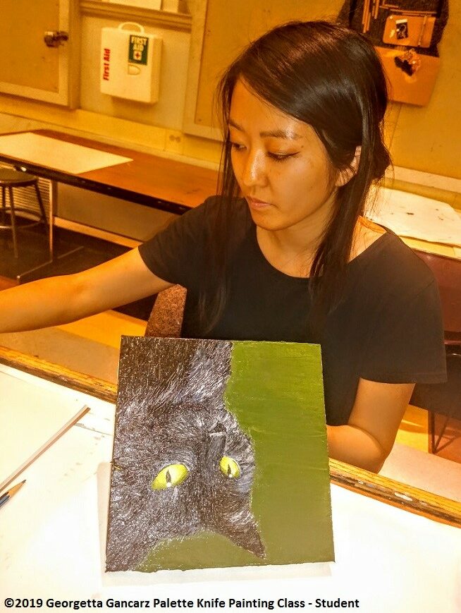 Student painting a black cat with yellow eyes 