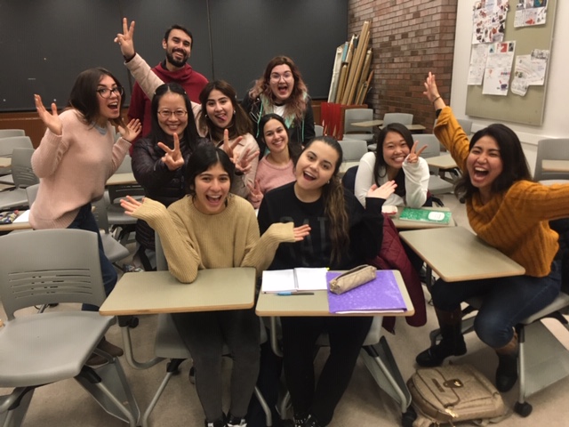 Au Pair students grouped around small desks with smiles and hands in the air - Continuing Education at Seattle Central College 