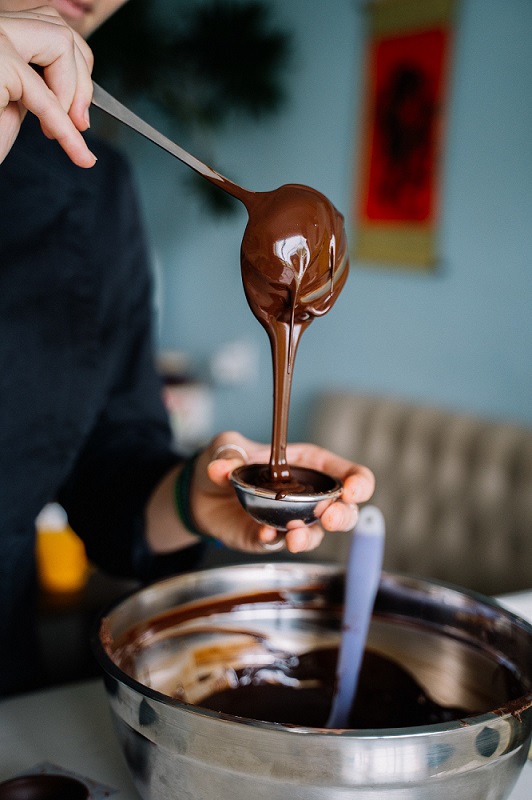 Chocolate Making from Bean to Bar class photo - Image of hands of person using a ladle pouring melted chocolate into a small cup over a pot (can't see face of person) - Continuing Education at Seattle Central College 