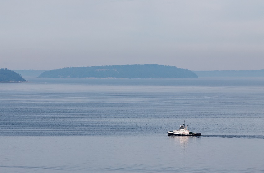 Photo of tug boat in the mid sea with land masses in distant background 
