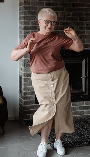 Photo of woman dancing with white hair, hands up, elbows out, long skirt and white tennis shoes 