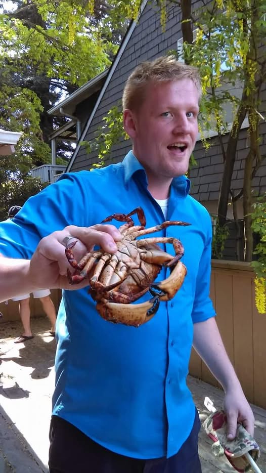 Instructor Will Oberst holding crab - fair sinned man grinning, wearing bright blue button up shirt. 