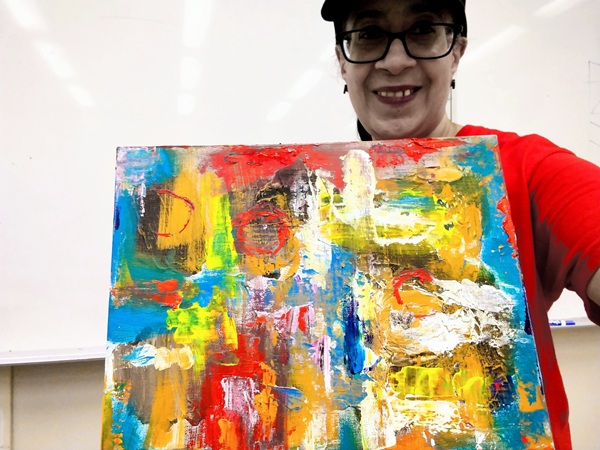 Woman in glasses holding colorful abstract painting.  