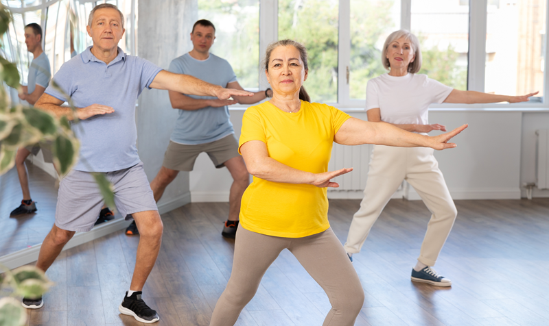 Group of older students bending one knee and reaching out with hands in Chi Kung pose. 