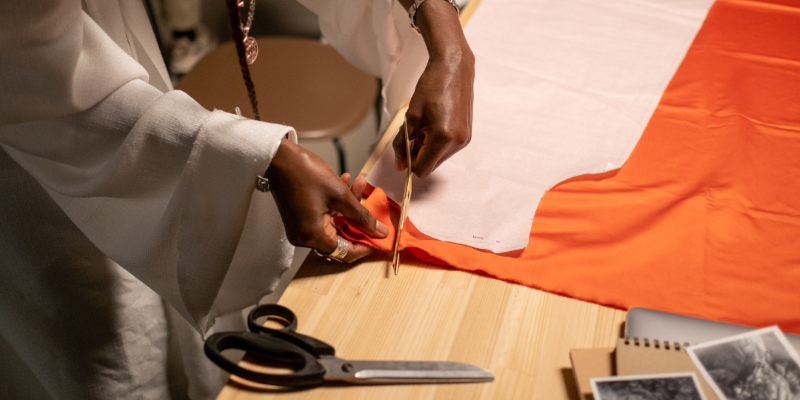 Hands pin orange fabric on cutting table.