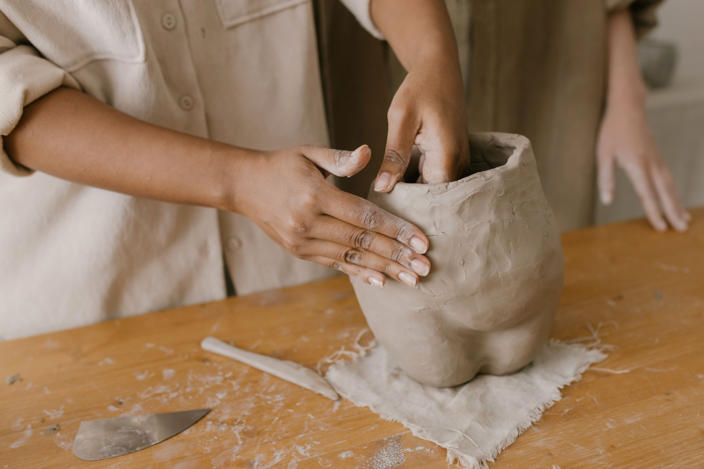 Two hands building clay vessel on table. 